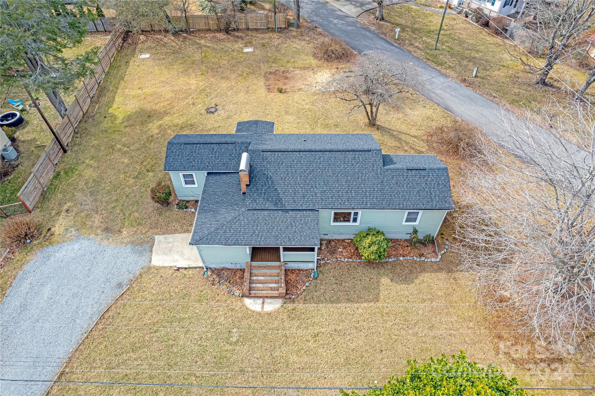 Aerial view of a light blue-gray home with a gravel driveway and fenced yard.