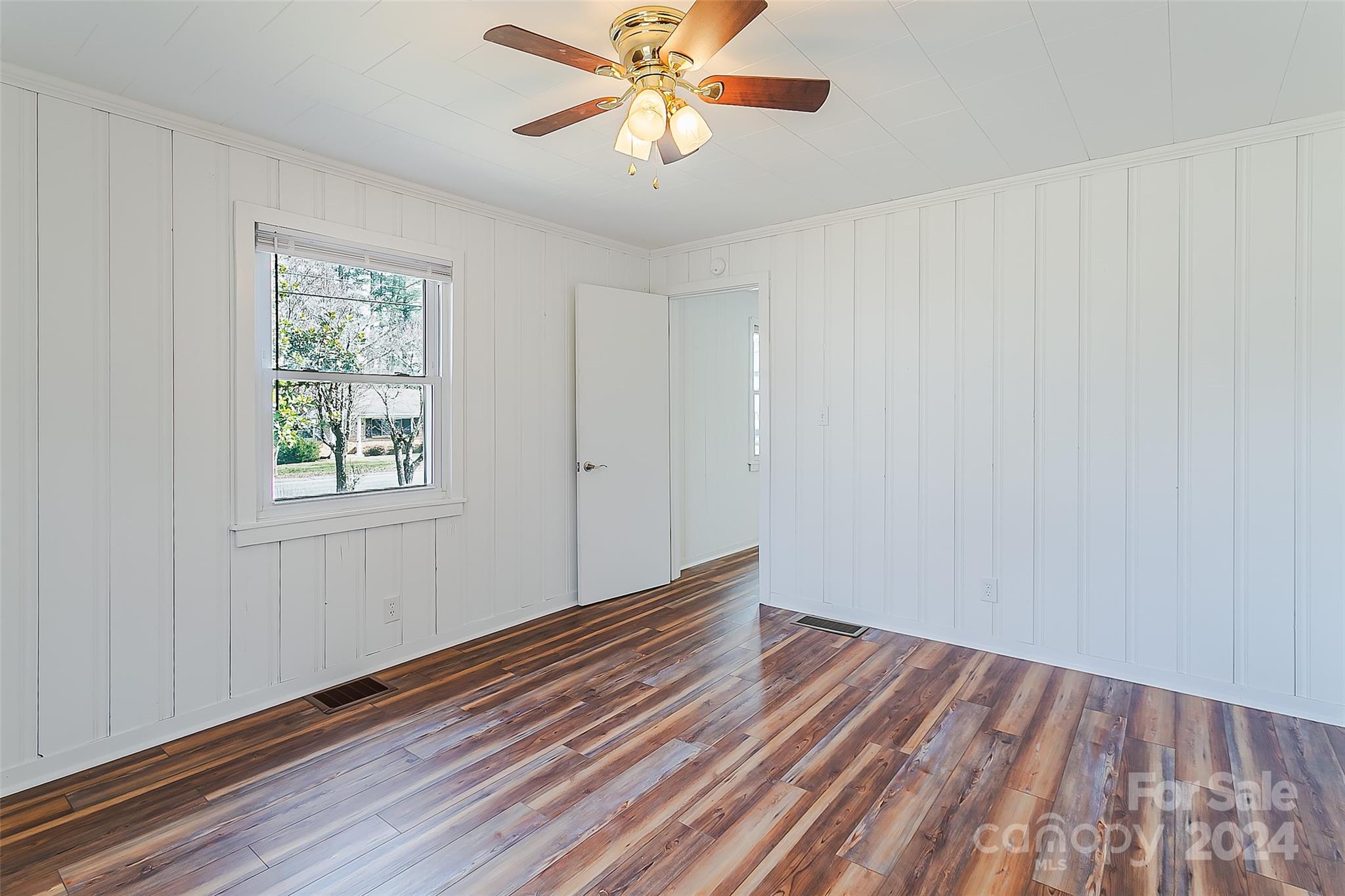 Vacant room with white paneled walls, a ceiling fan, and multicolored wood-look flooring.
