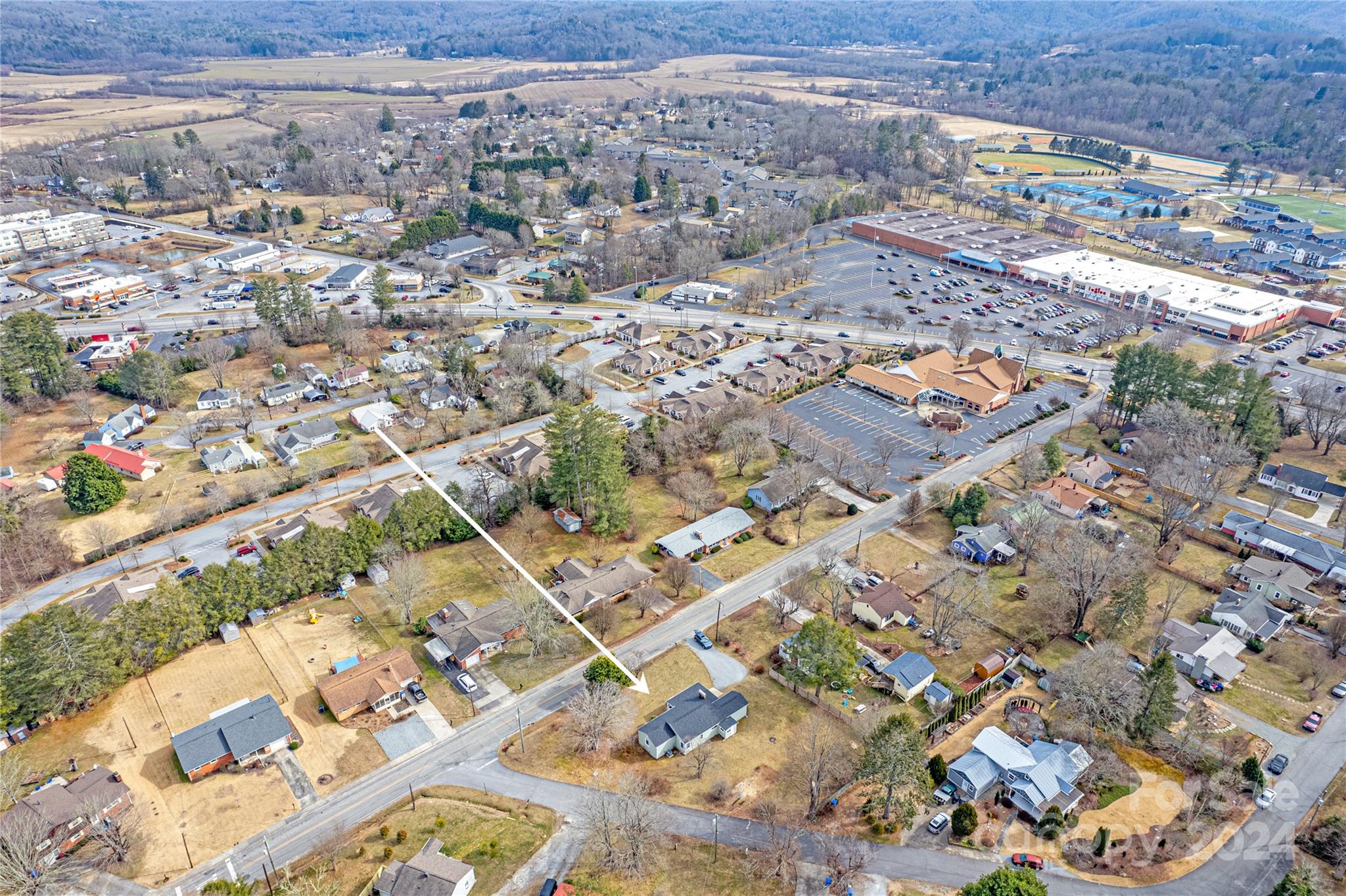 Aerial neighborhood view with an arrow pointing to a gray-roofed house beside the road.