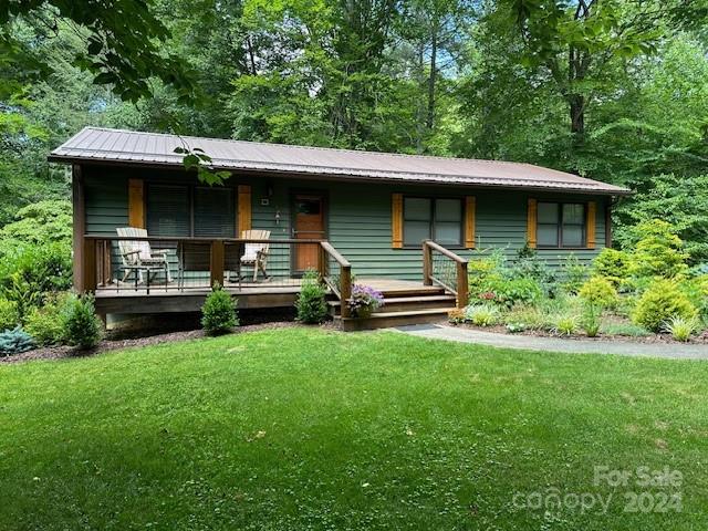 Green single-story house with a raised front porch, surrounded by trees and lawn.