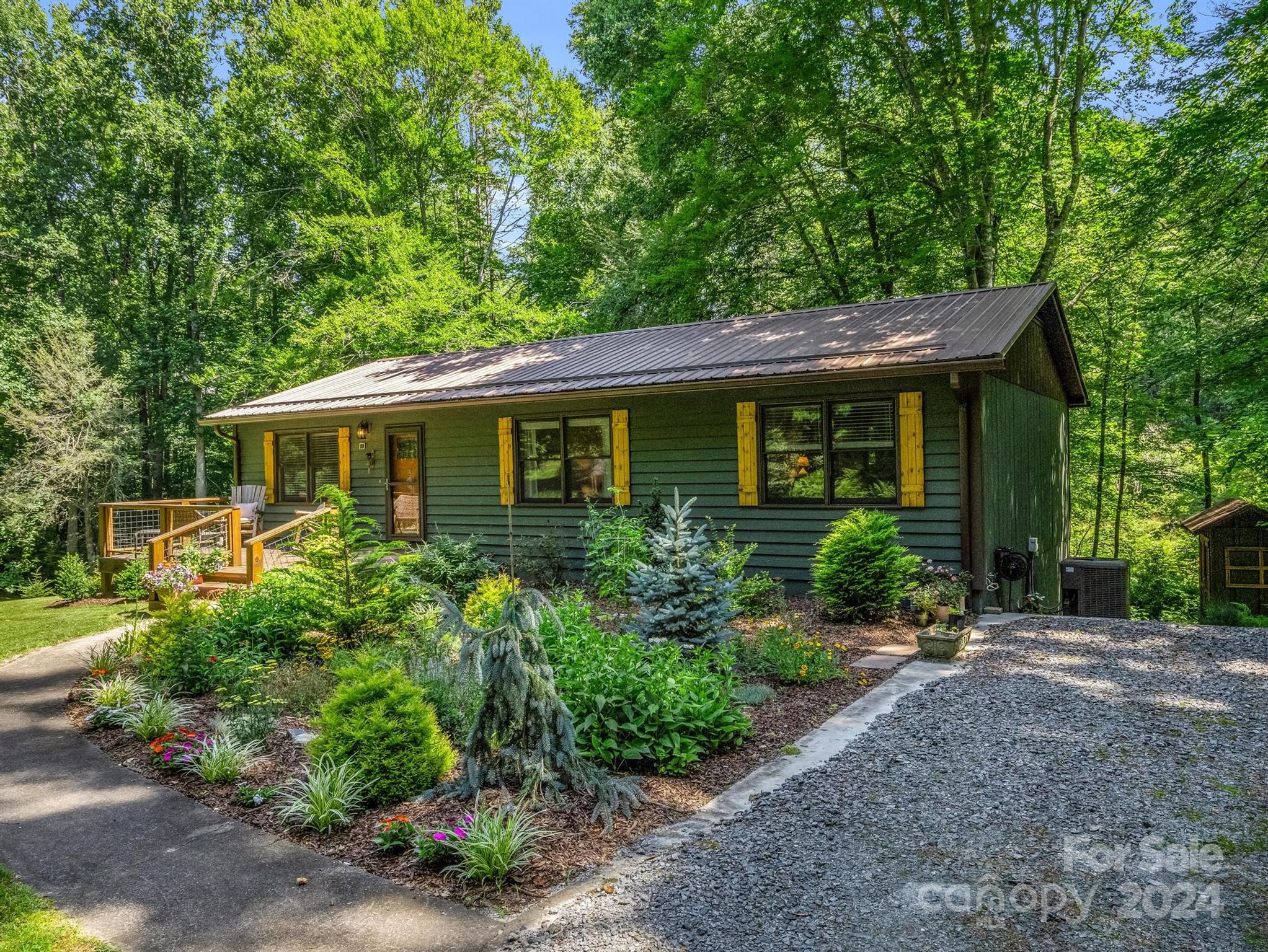 Green house with yellow shutters, a metal roof, landscaped gardens, and a small wooden deck.
