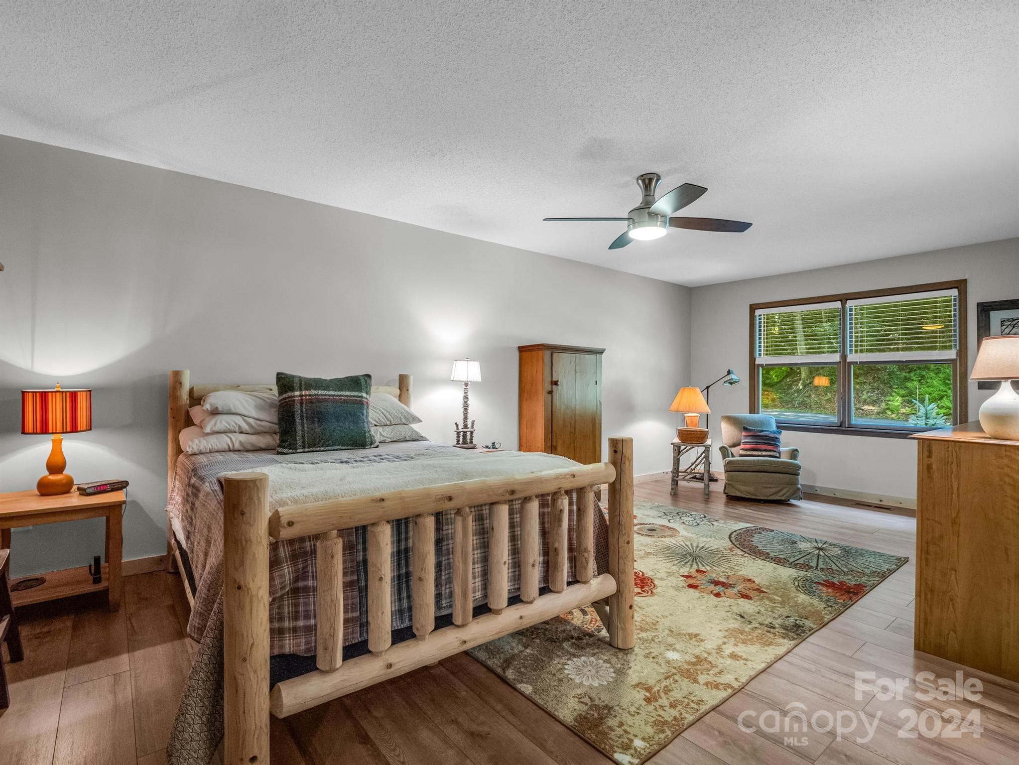 Bedroom with a rustic log bed, patterned rug, and windows overlooking greenery.