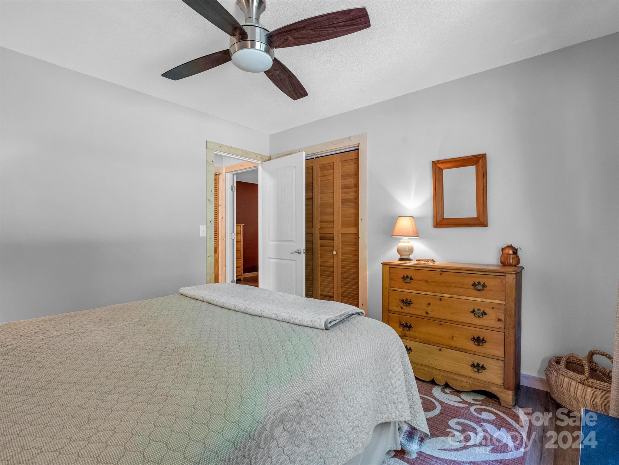 Furnished bedroom with a large bed, wooden dresser, and ceiling fan.
