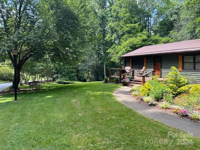 Wooded home with a red metal roof, front deck, and curved garden path beside a broad lawn.