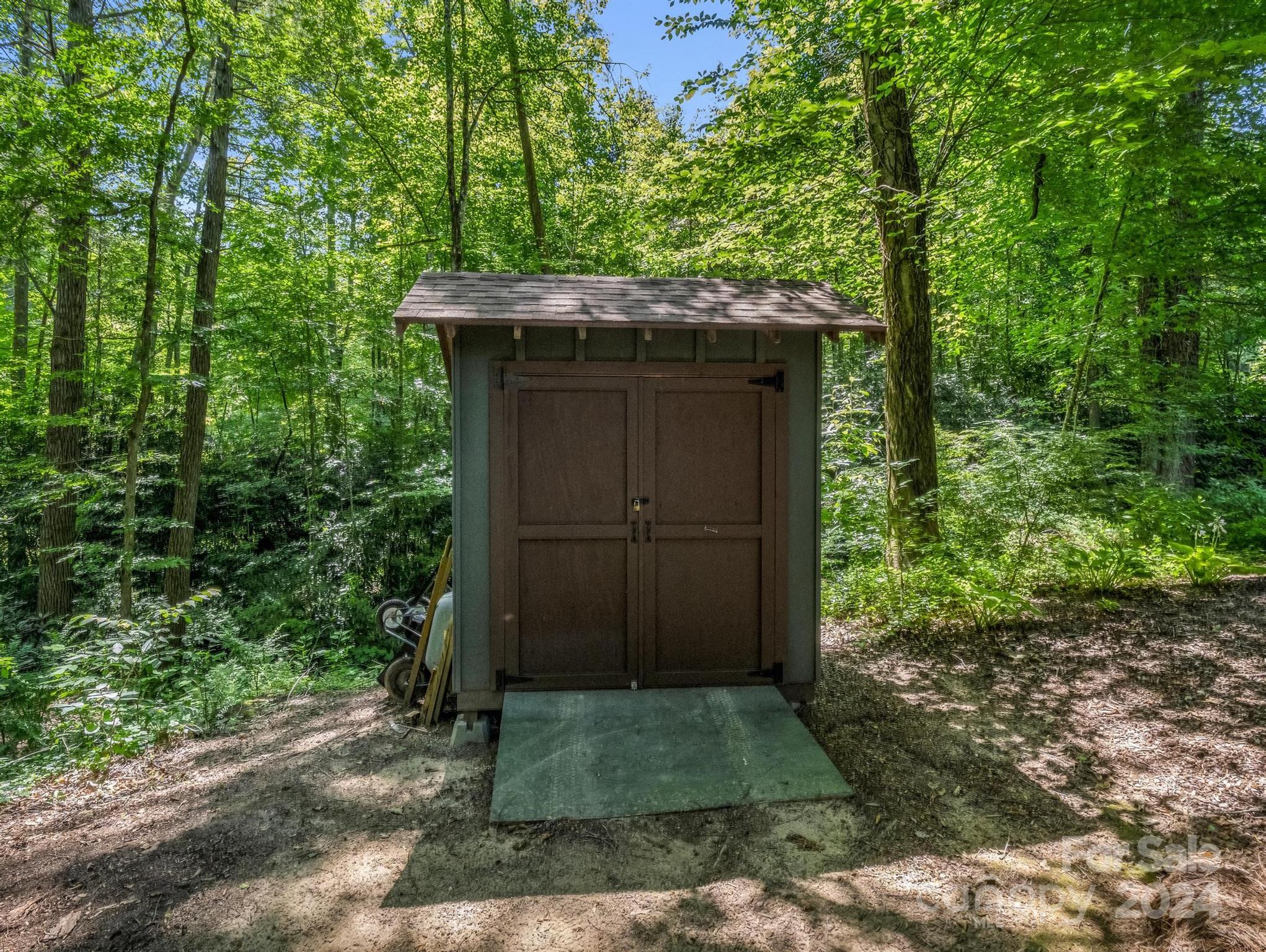 Brown double-door storage shed with a concrete pad in a wooded yard.