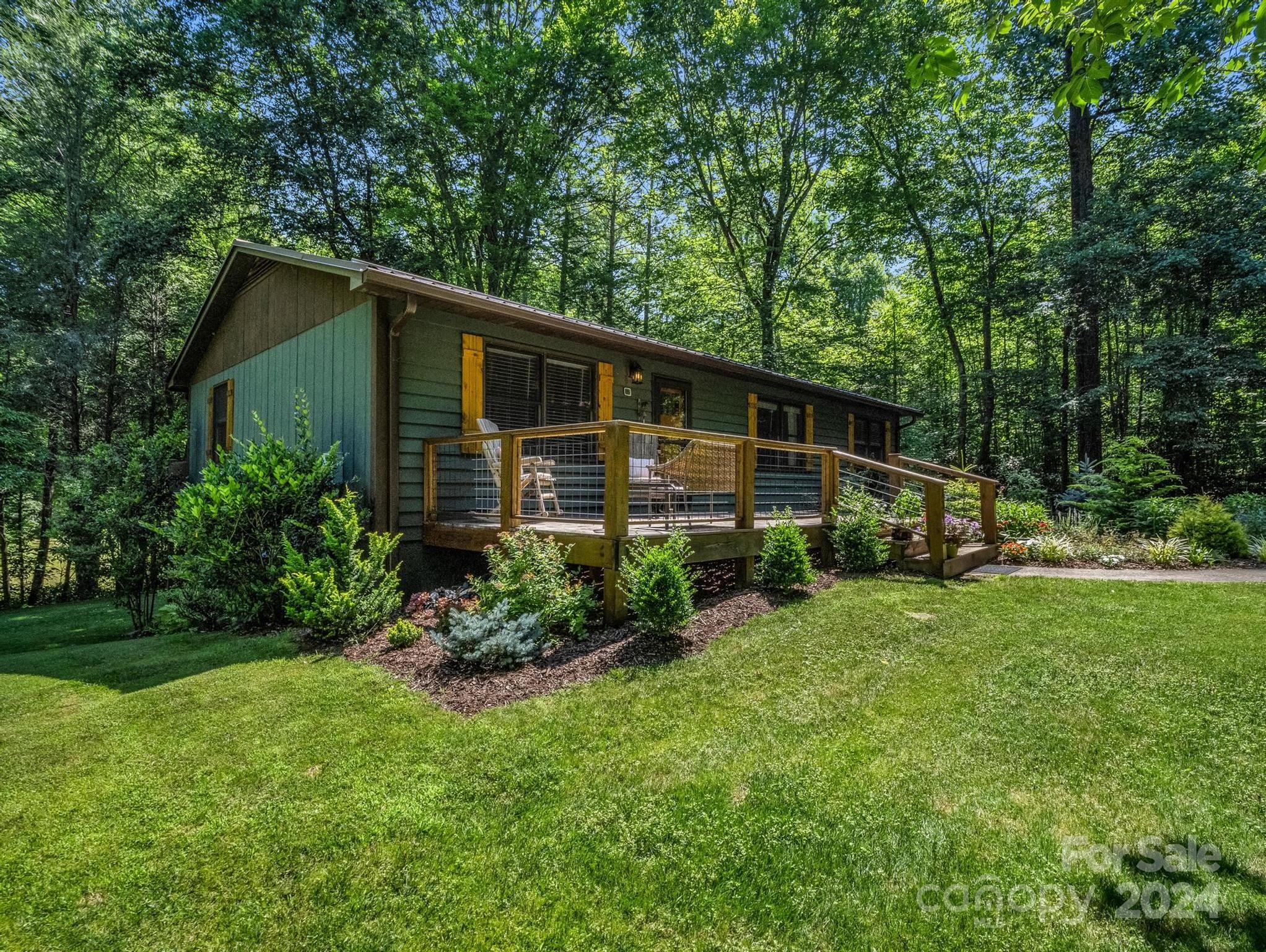 Wooded home with a raised deck, outdoor seating, landscaped garden, and broad lawn.