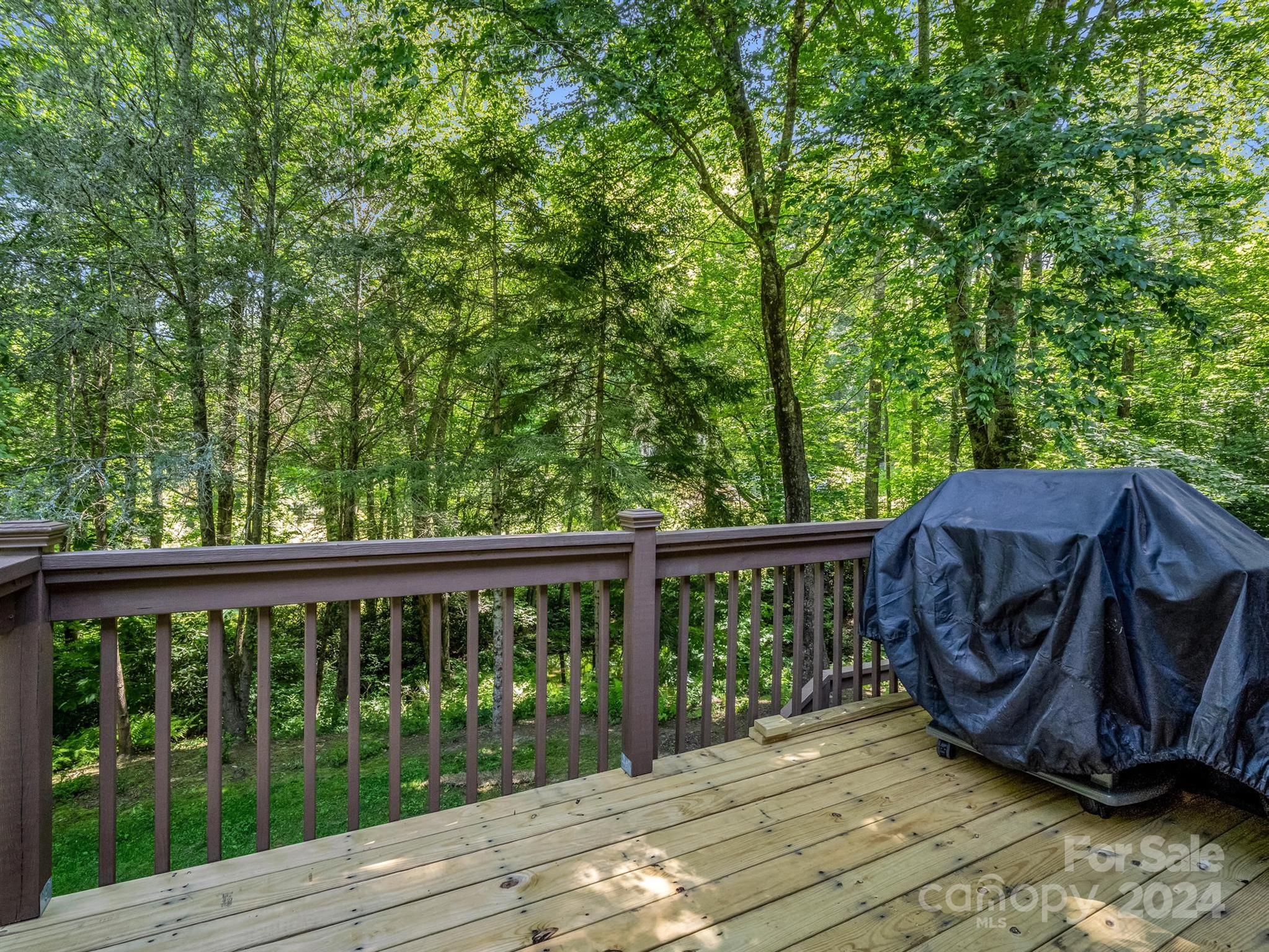Wooden deck overlooking dense woodland, with a covered grill beside the railing.