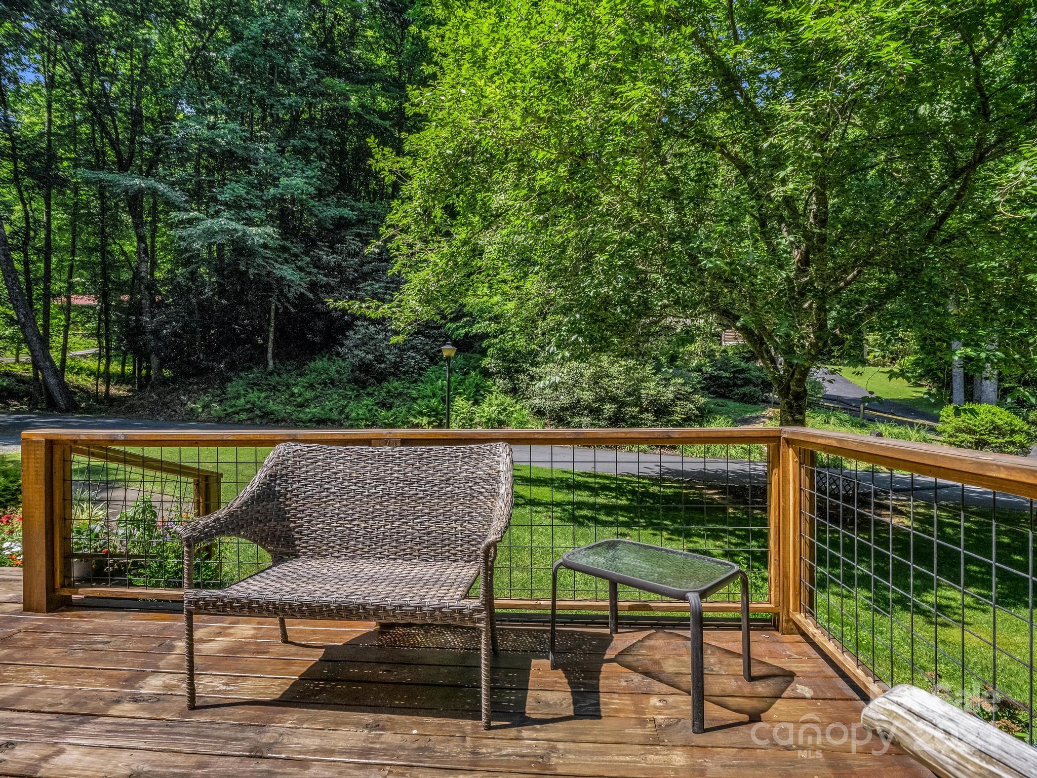 Wooden deck with a wicker lounge chair and side table overlooking a leafy yard.