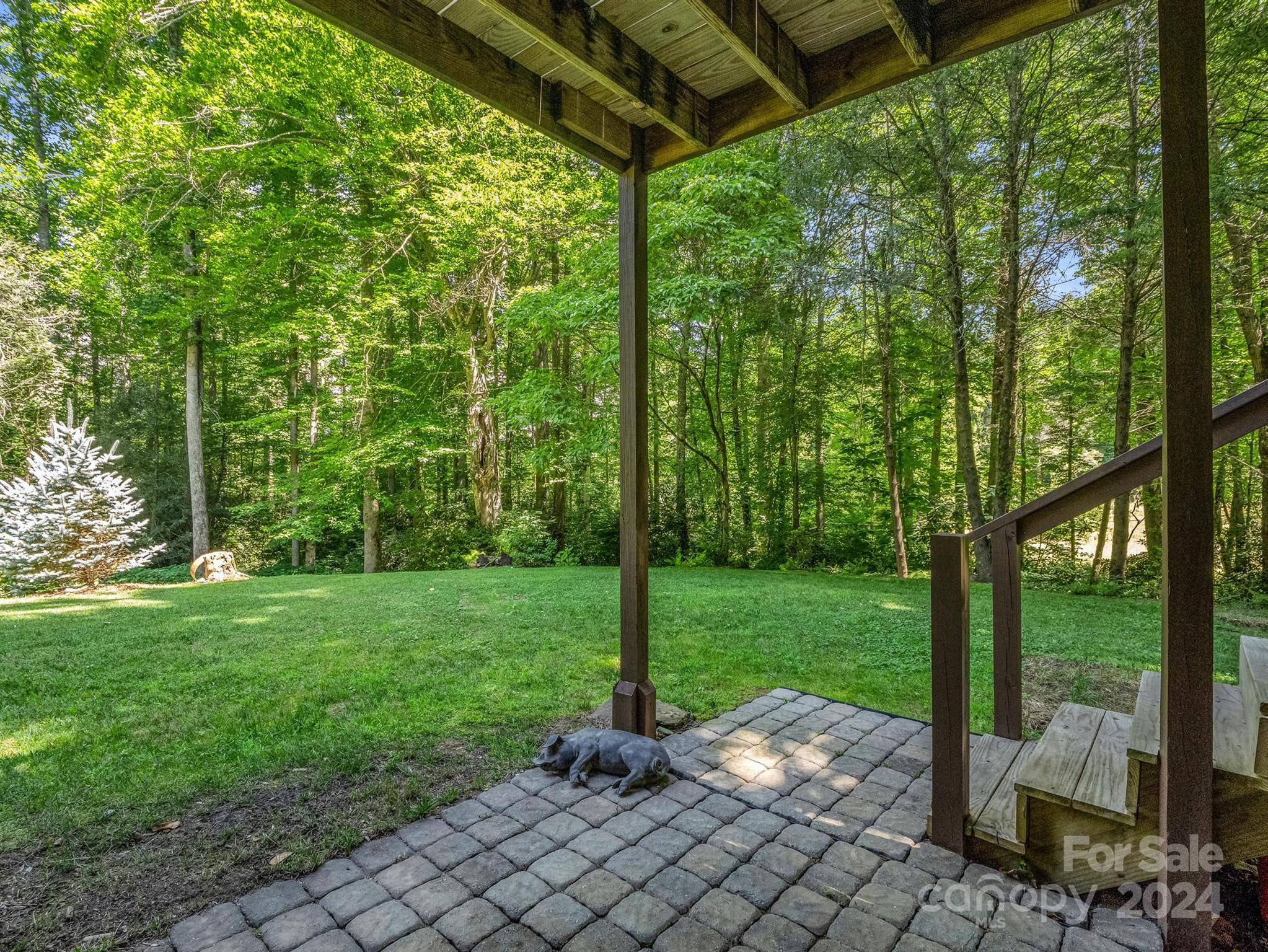 Covered patio with stone pavers and wooden steps overlooking a grassy, wooded yard.
