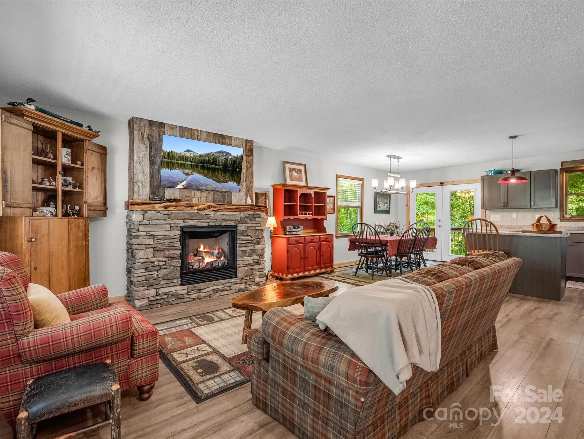Living room with a stone fireplace, plaid sofas, and an adjoining dining area and kitchen.