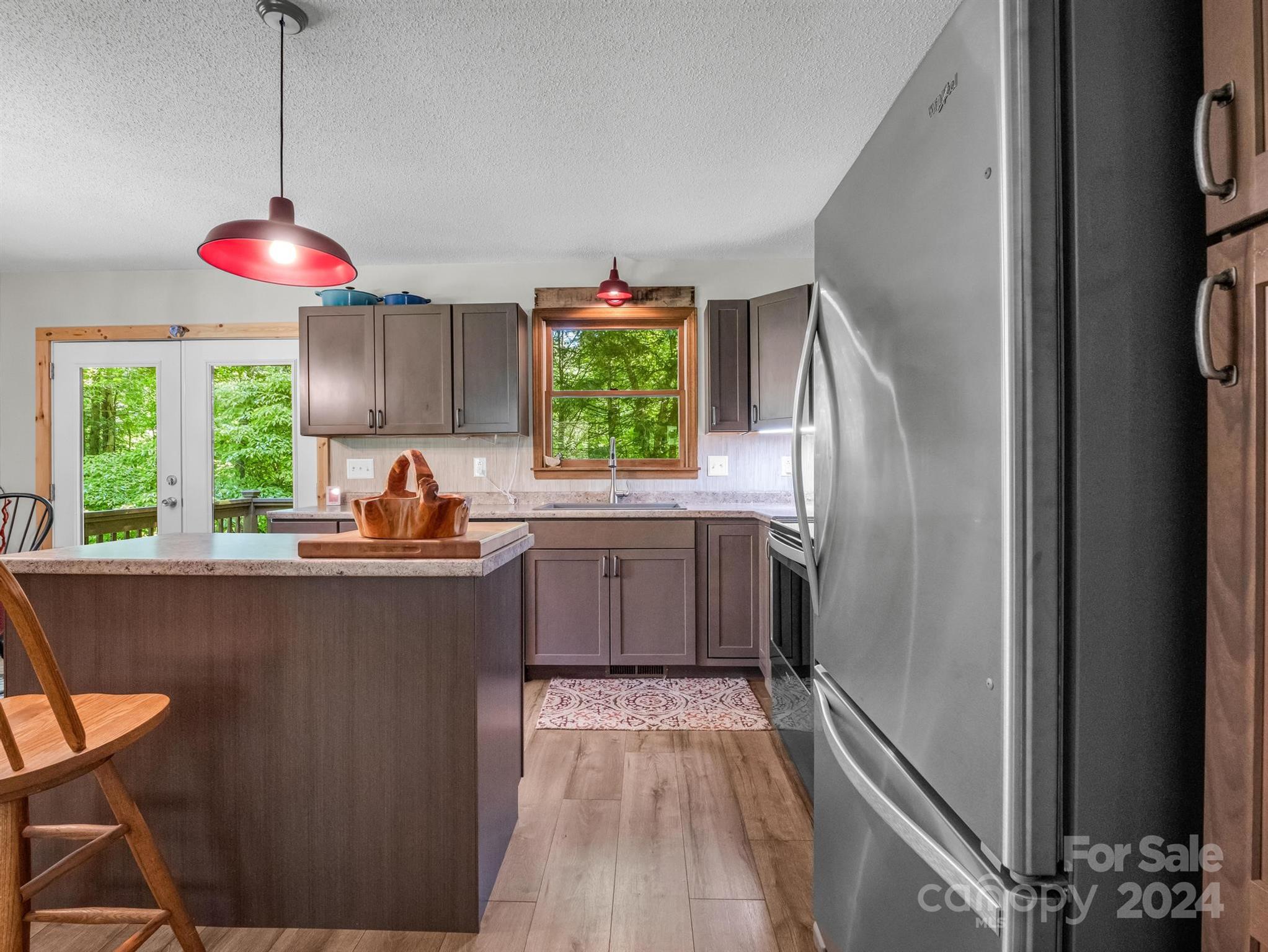 Kitchen with a large island, red pendant lights, and windows overlooking green trees.