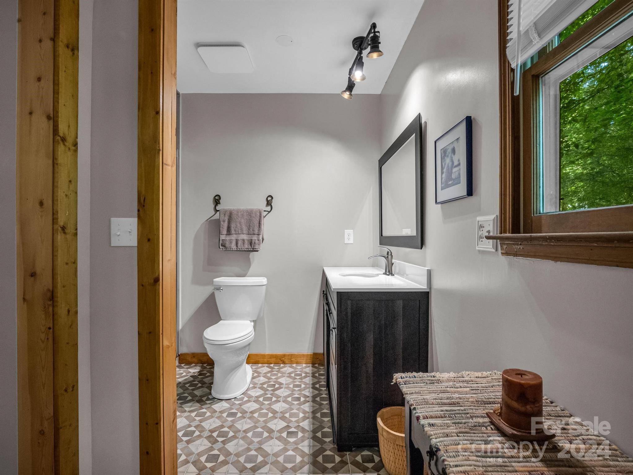 Bathroom with a dark vanity, geometric tile floor, and wood-trimmed window.