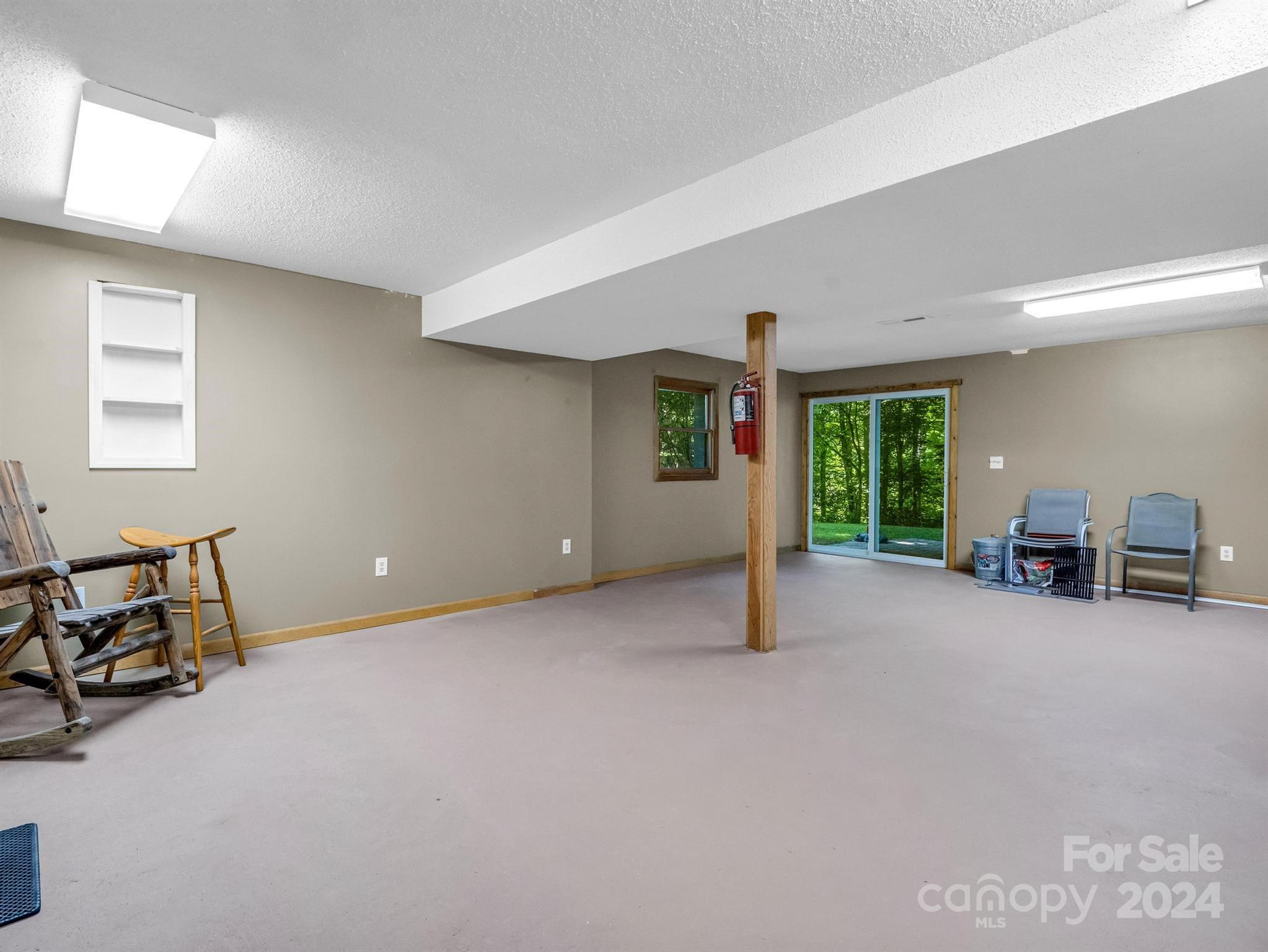 Carpeted basement room with a wooden support post and sliding glass doors overlooking trees.