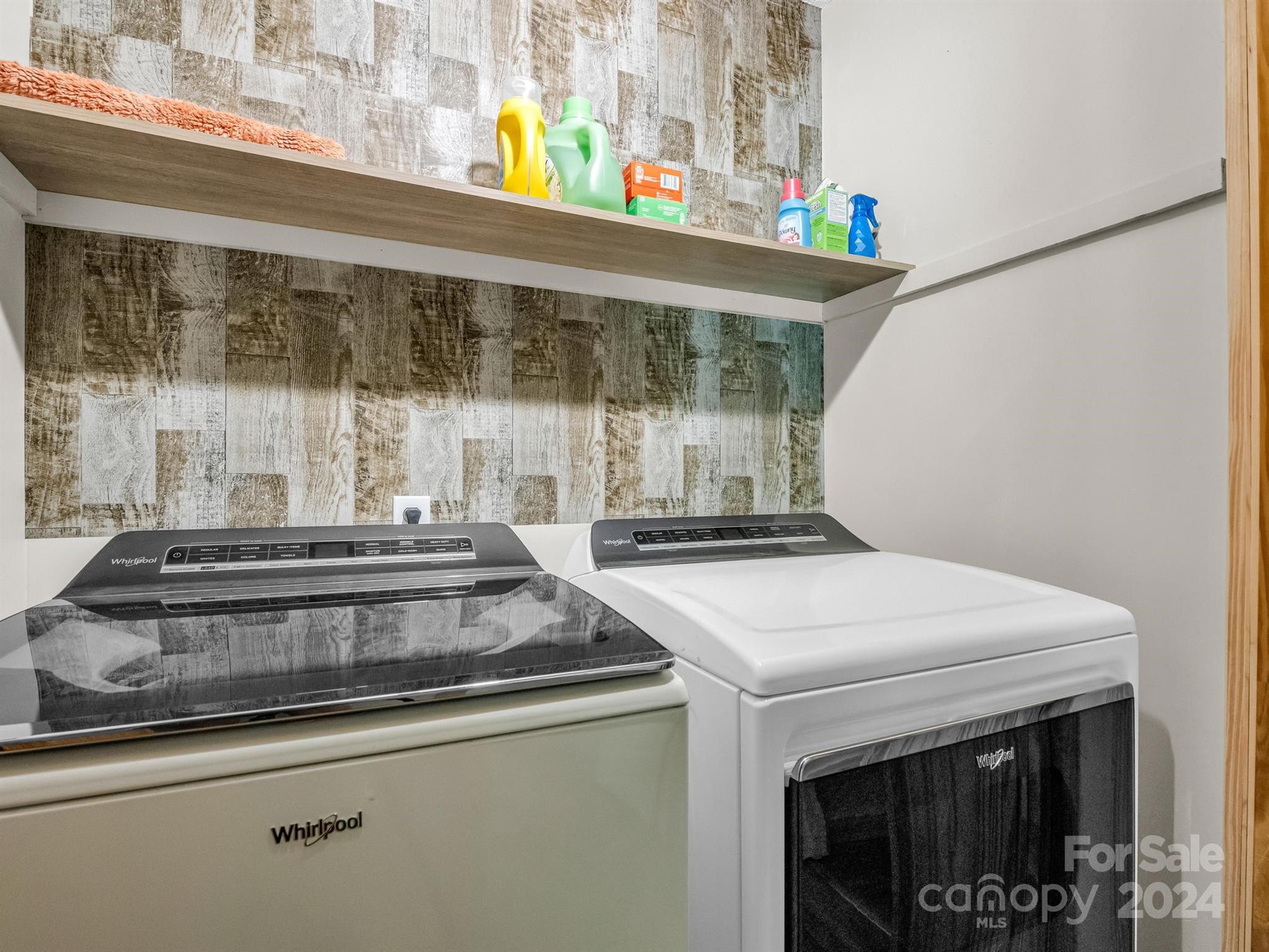 Laundry room with Whirlpool washer and dryer beneath a shelf of cleaning supplies.