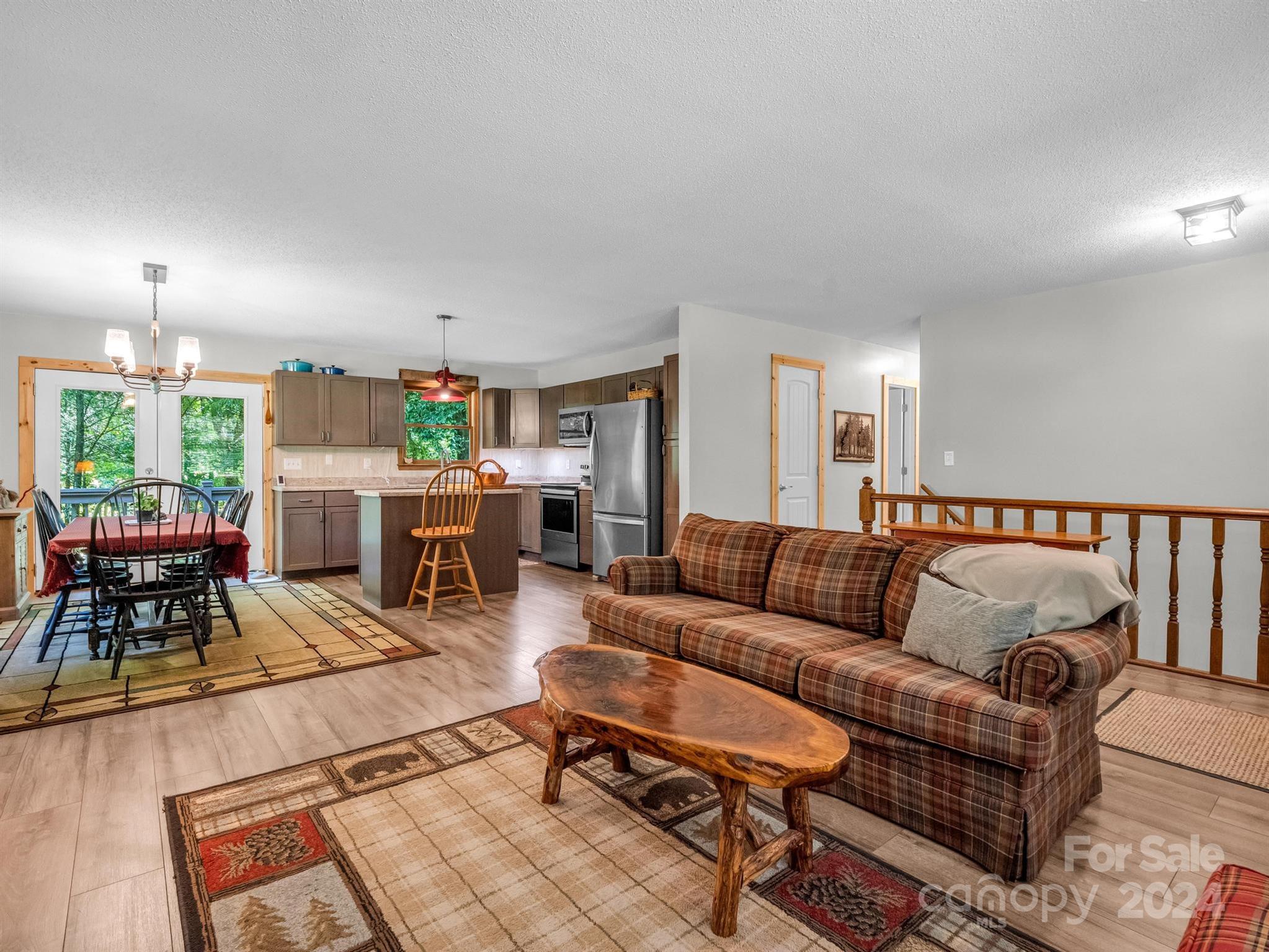 Open-plan living room with a plaid sofa, rustic coffee table, and kitchen with stainless steel appliances.