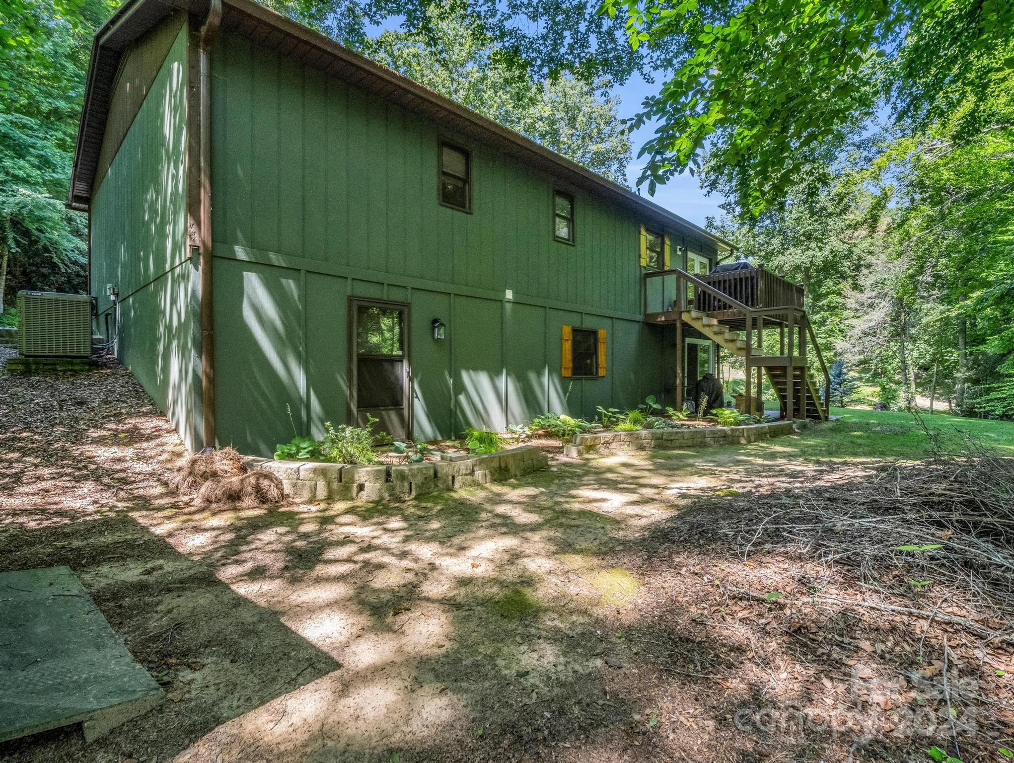 Green two-story home in a wooded yard, with a raised deck and exterior stairs.