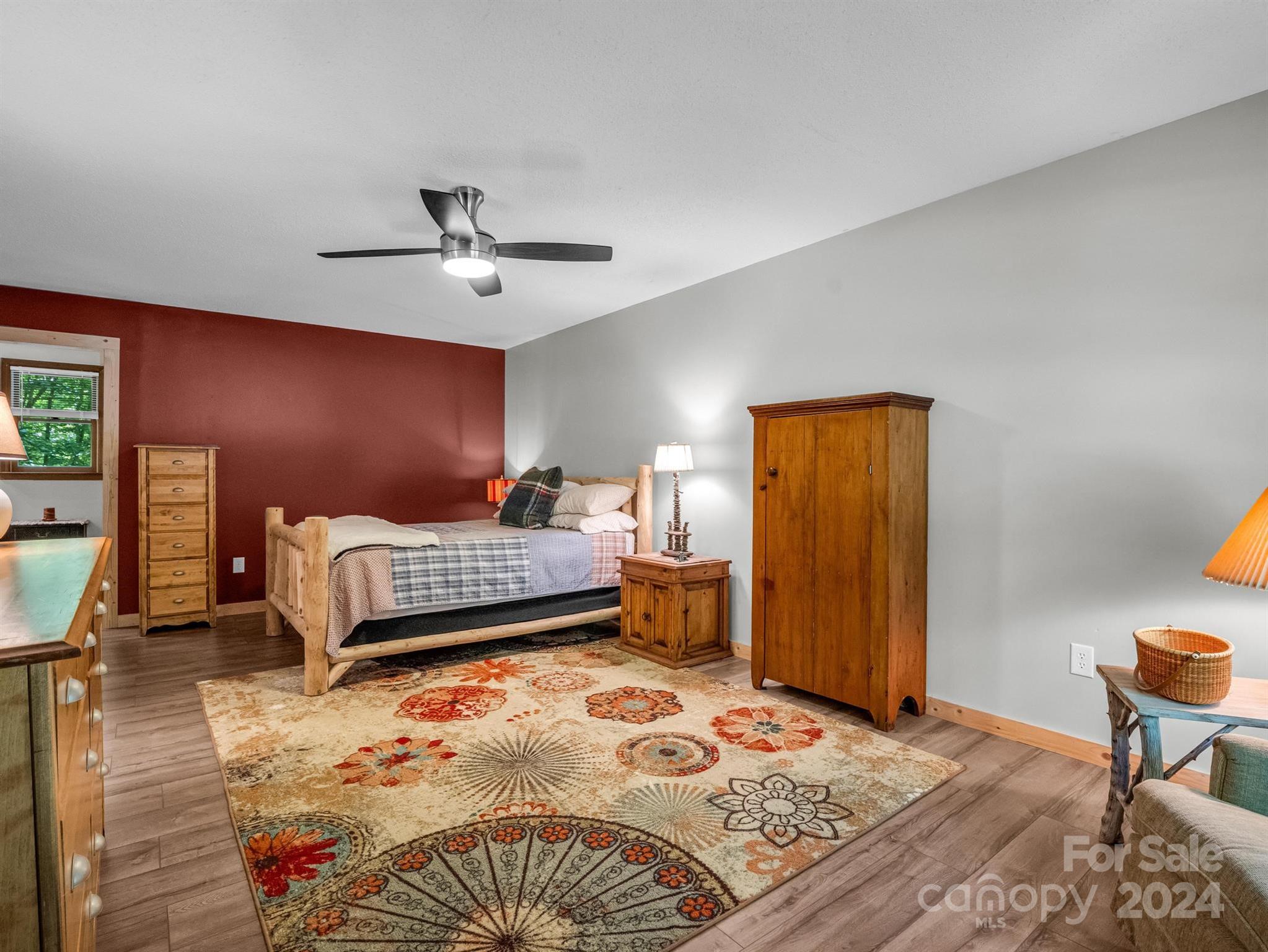 Bedroom with a rustic wooden bed, red accent wall, and large floral-patterned rug.