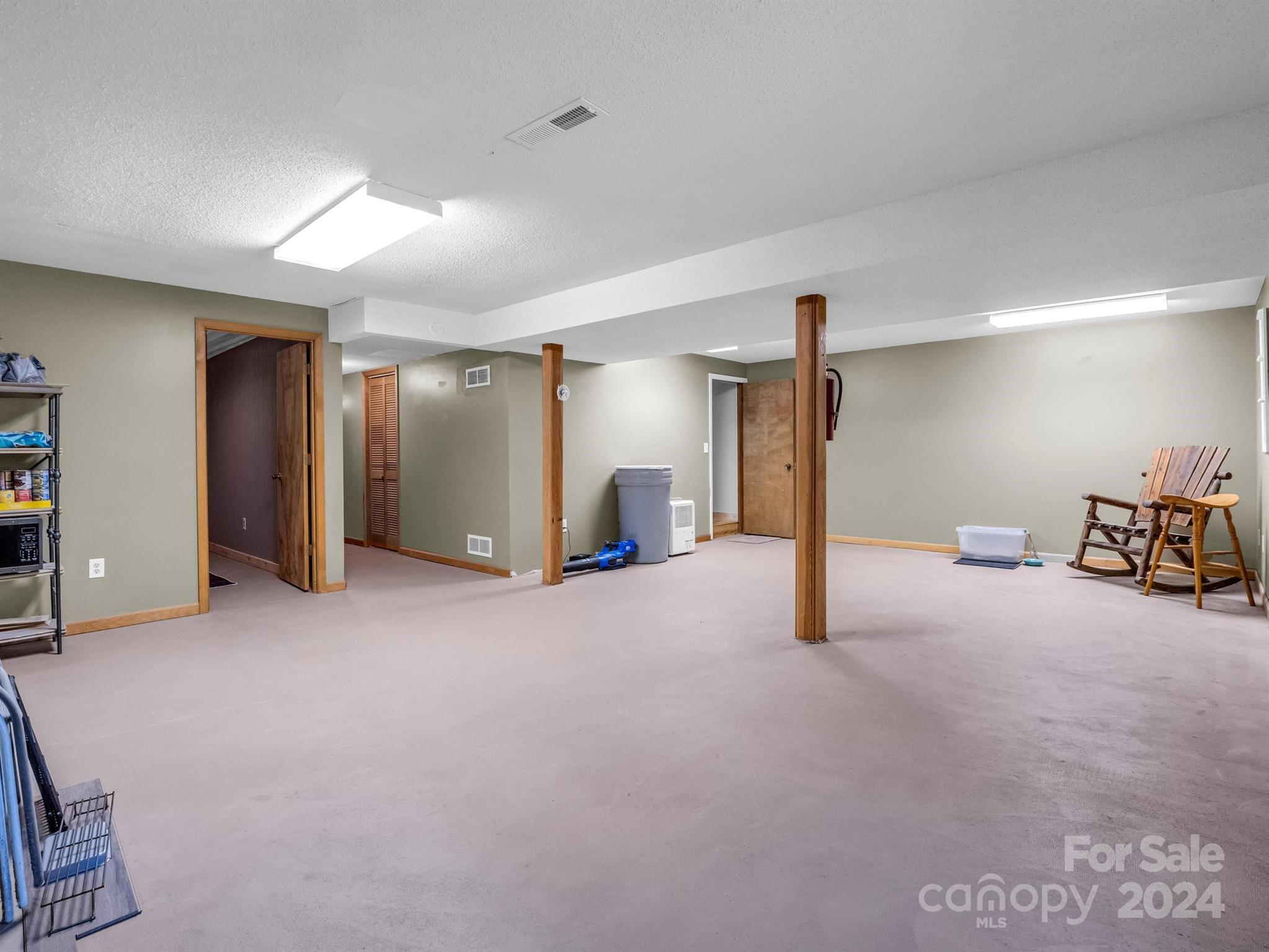 Spacious carpeted basement with wooden support posts and rocking chairs.