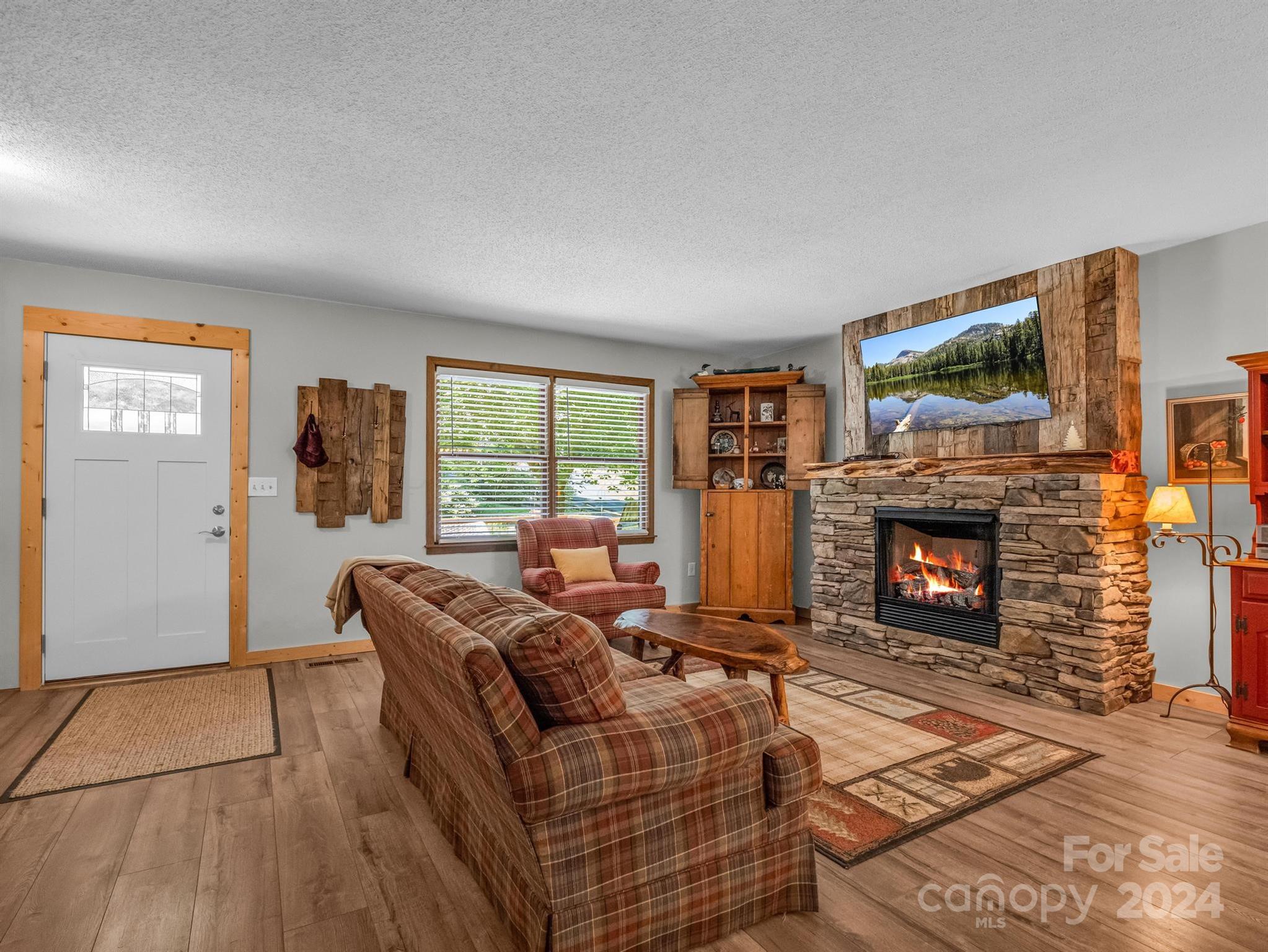 Living room with a stone fireplace, plaid seating, and rustic wood cabinetry.