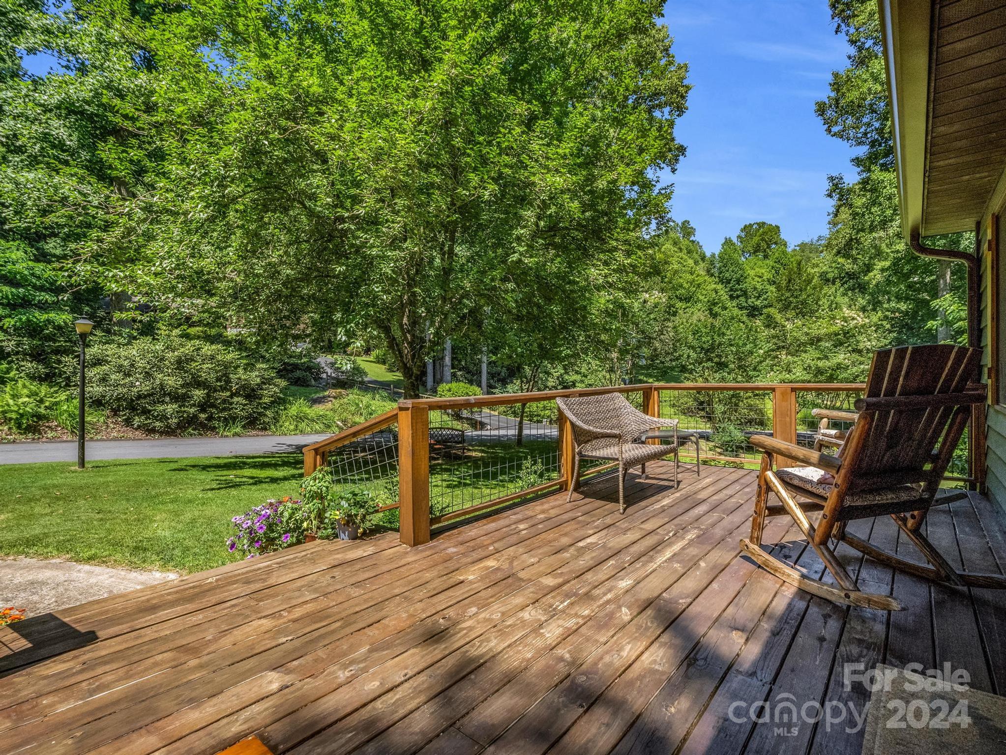 Wooden deck with two chairs overlooking a green lawn and wooded yard.