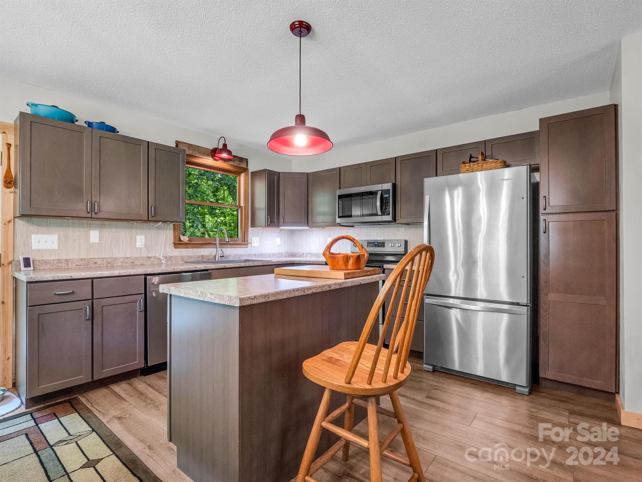Kitchen with dark cabinets, stainless steel appliances, and an island beneath red pendant lights.