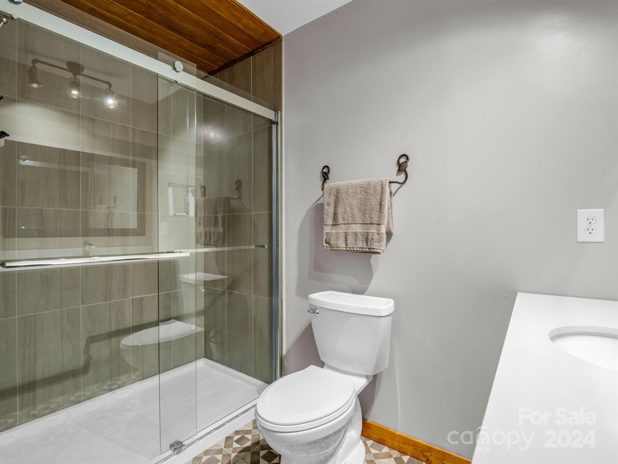 Bathroom with glass-enclosed shower, wood ceiling, and geometric patterned floor tile.