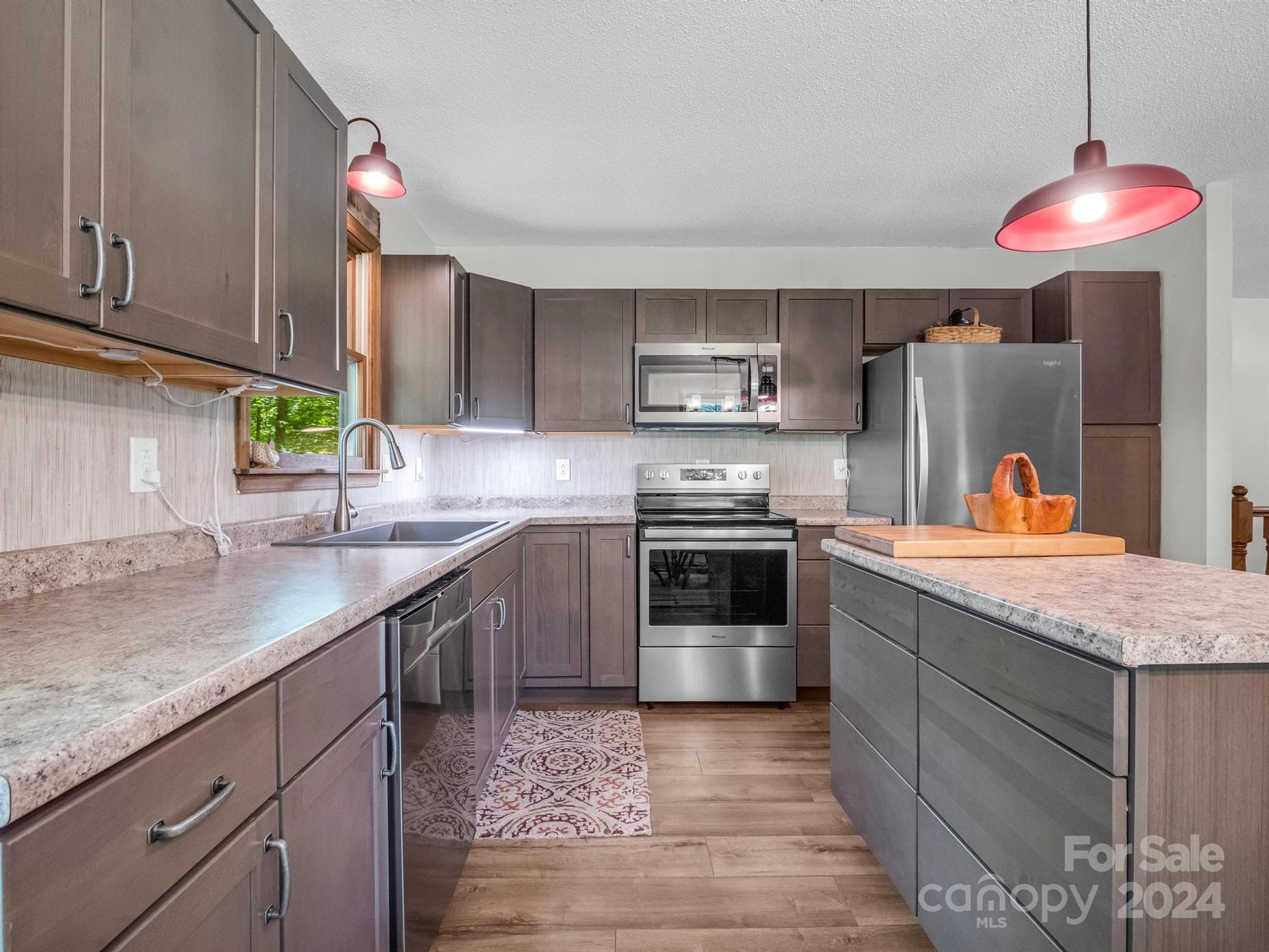 Kitchen with dark cabinets, granite counters, stainless steel appliances, and red pendant lights.