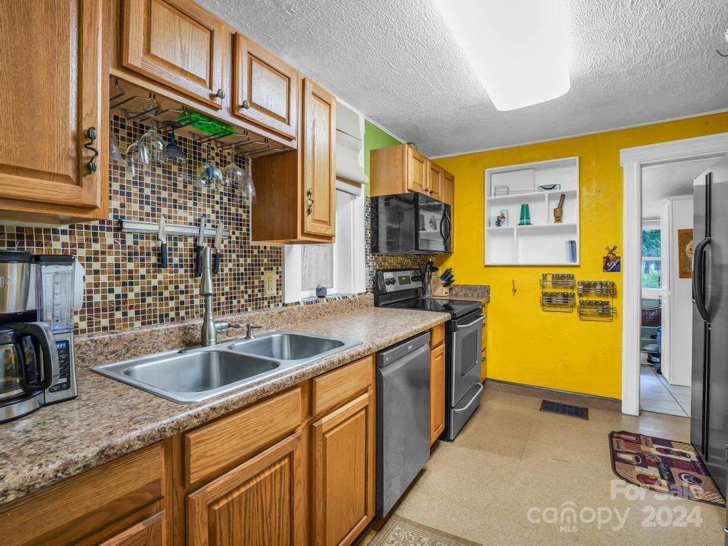 Kitchen with wood cabinetry, mosaic backsplash, granite counters, and stainless steel appliances.