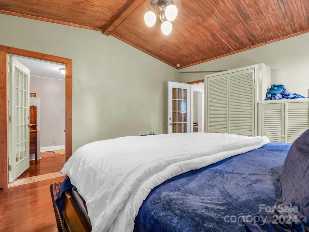 Bedroom with a blue bedspread, louvered closets, and a high wood-paneled ceiling.