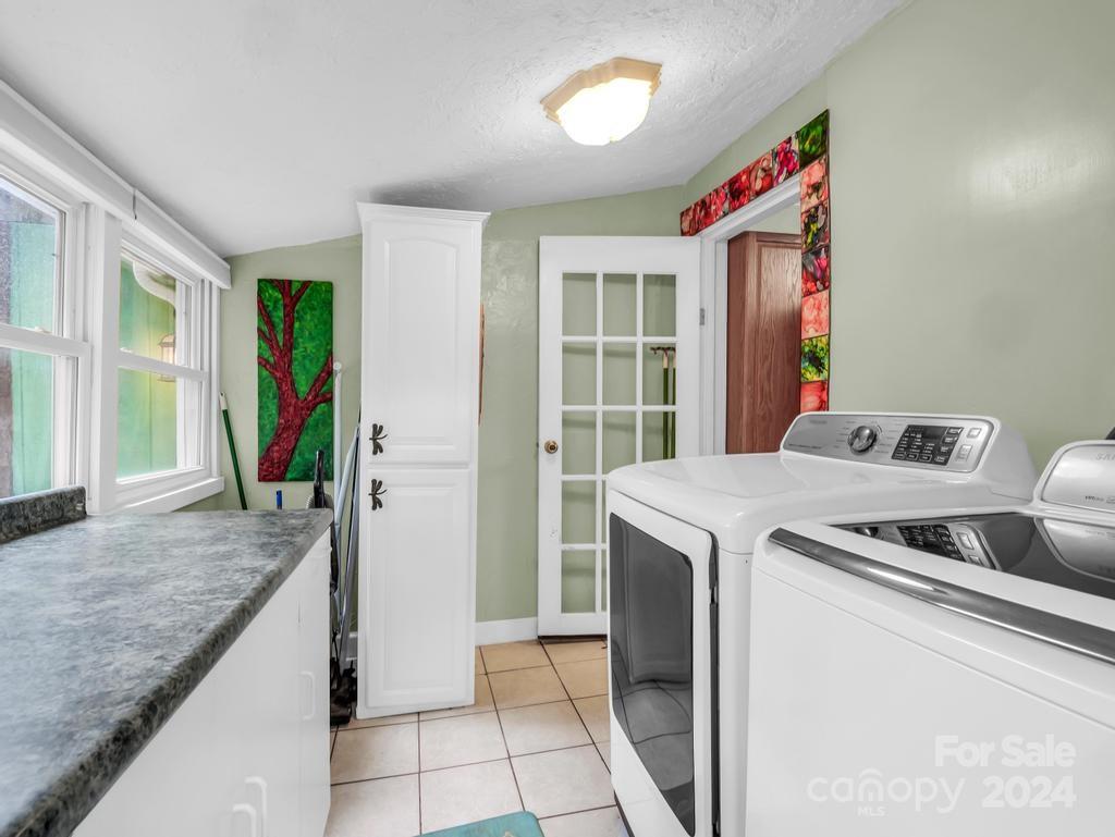 Laundry room with white washer and dryer beside a stone counter and windows.