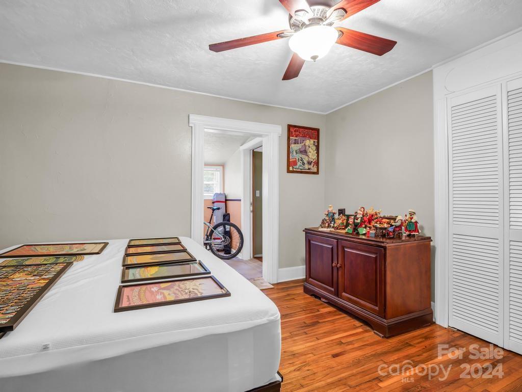 Bedroom with hardwood floors, a ceiling fan, and a wooden cabinet displaying holiday figurines.