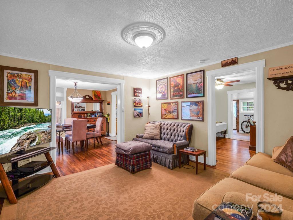Furnished living room with a tufted loveseat, patterned ottoman, hardwood floors, and doorways to adjoining rooms.