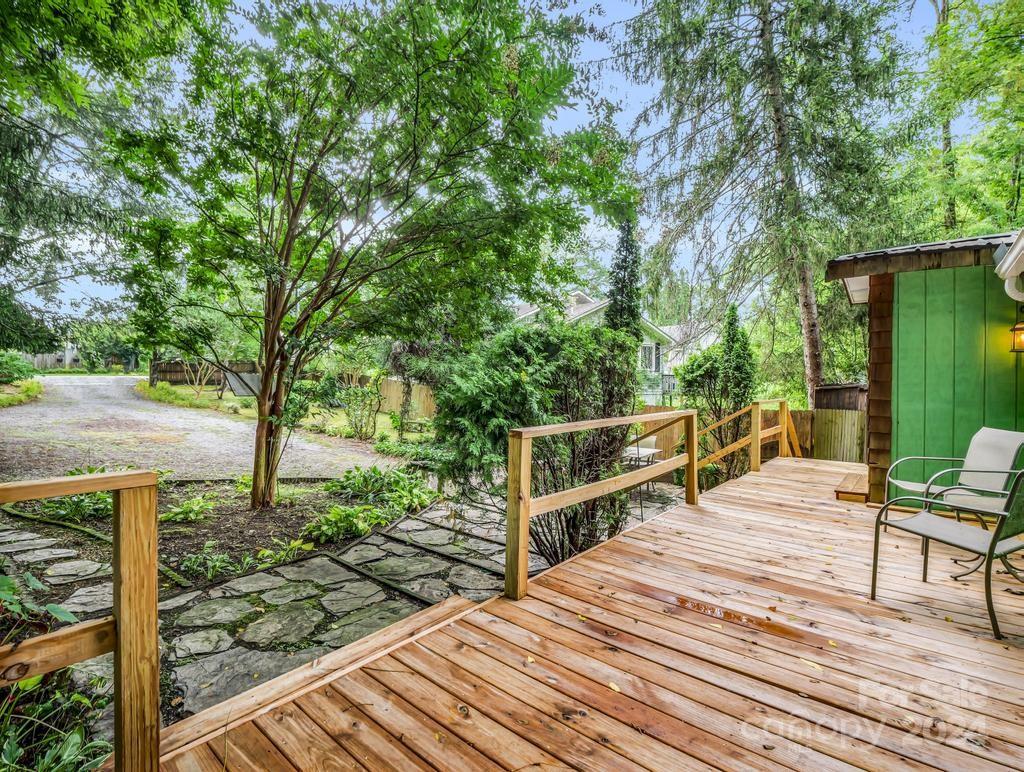 Wooden deck beside a green outbuilding, with chairs, stone pavers, and a leafy yard.