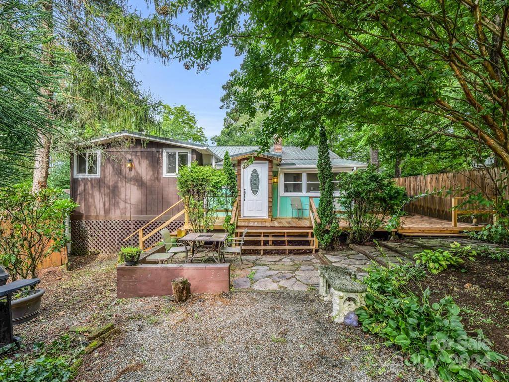 Home framed by mature trees, with a stone patio and wooden deck steps leading to the front door.