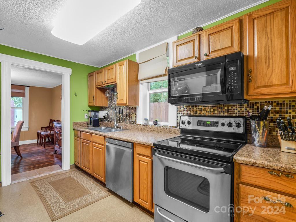 Kitchen with honey-colored cabinets, stainless appliances, patterned backsplash, and a doorway to the dining room.