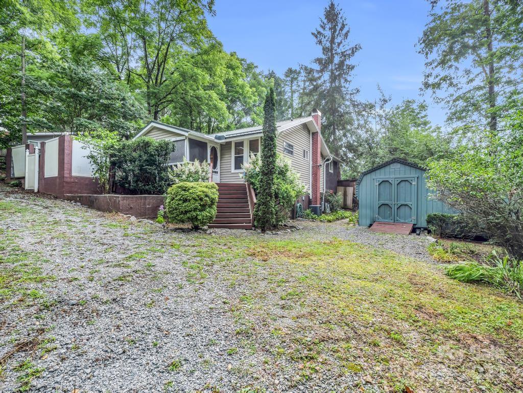 Single-story house with front steps and a blue garden shed among trees.