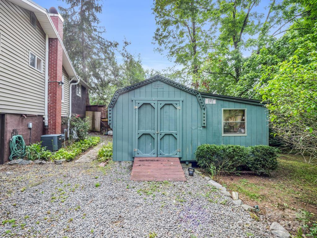 Teal storage shed with double doors and a wooden ramp beside a house.