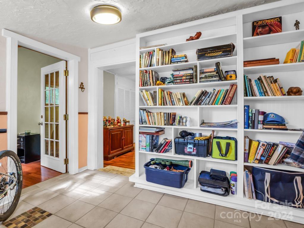 Built-in white bookshelves filled with books and storage bins beside a tiled floor and open doorways.