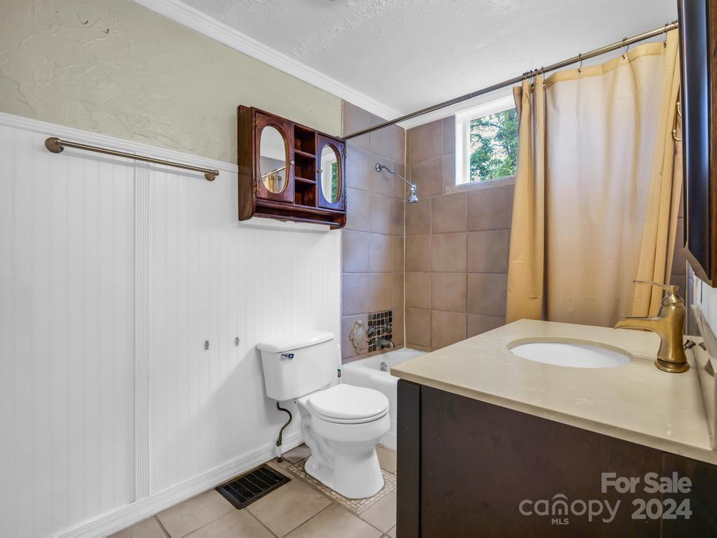 Bathroom with tiled tub and shower, yellow curtain, white toilet, and dark vanity.