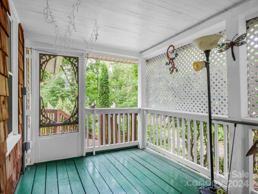 Covered porch with teal floorboards, white lattice panels, and leafy greenery beyond the railing.