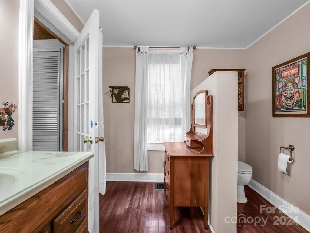 Bathroom with a wood vanity, matching dresser, and toilet behind a privacy partition.