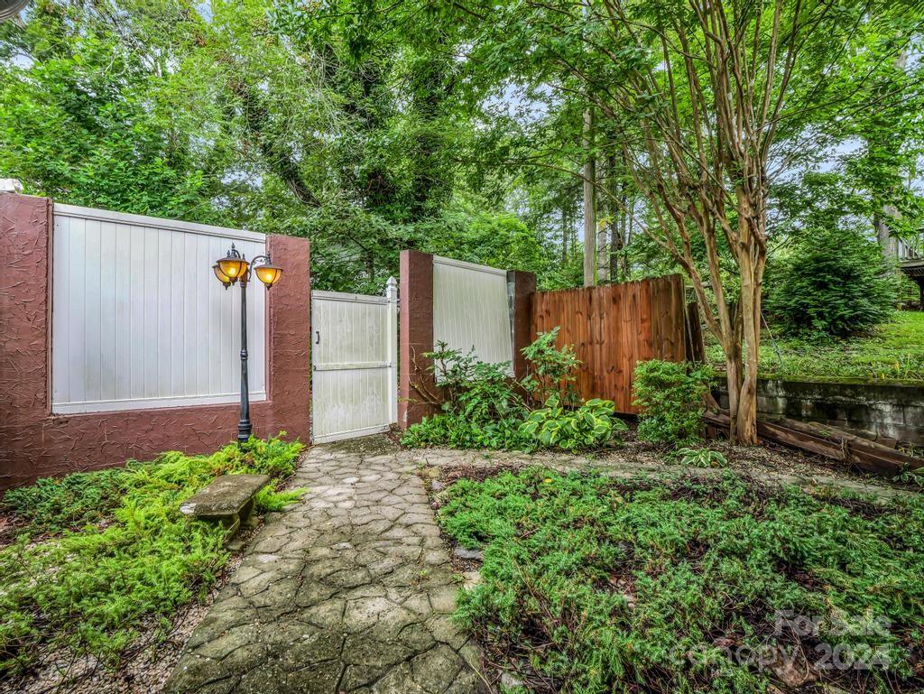 Landscaped entrance with a stone path leading to a white gate beneath mature trees.