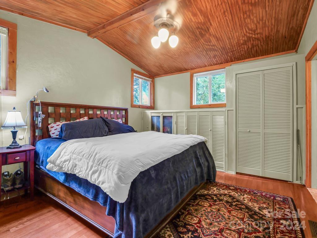 Bedroom with a vaulted wood-plank ceiling, louvered closets, and a bed with a white comforter.