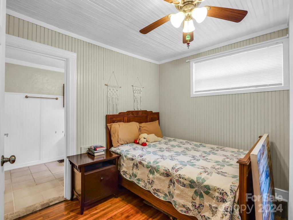 Bedroom with a dark wood bed, patterned quilt, ceiling fan, and open doorway to a tiled bathroom.