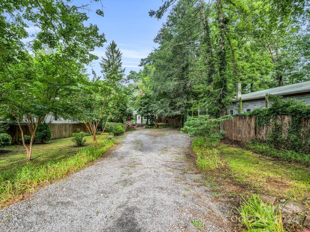 Gravel driveway leading to a home beneath mature trees, with wooden fencing and landscaped borders.