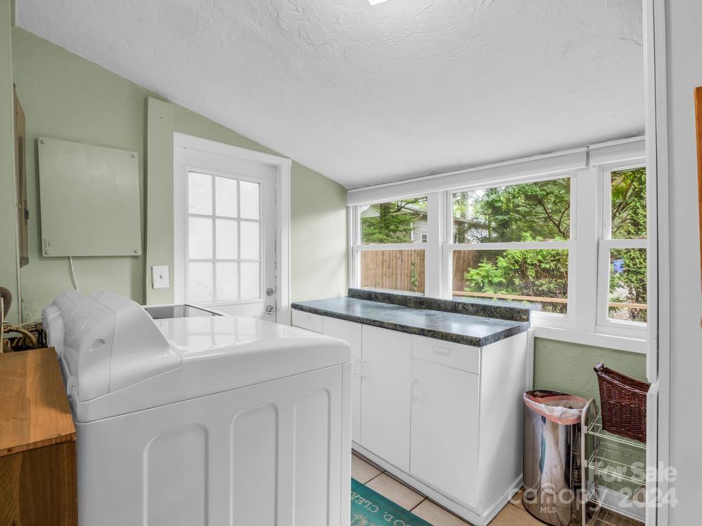 Laundry room with white washer and dryer, dark countertop, and large windows overlooking greenery.