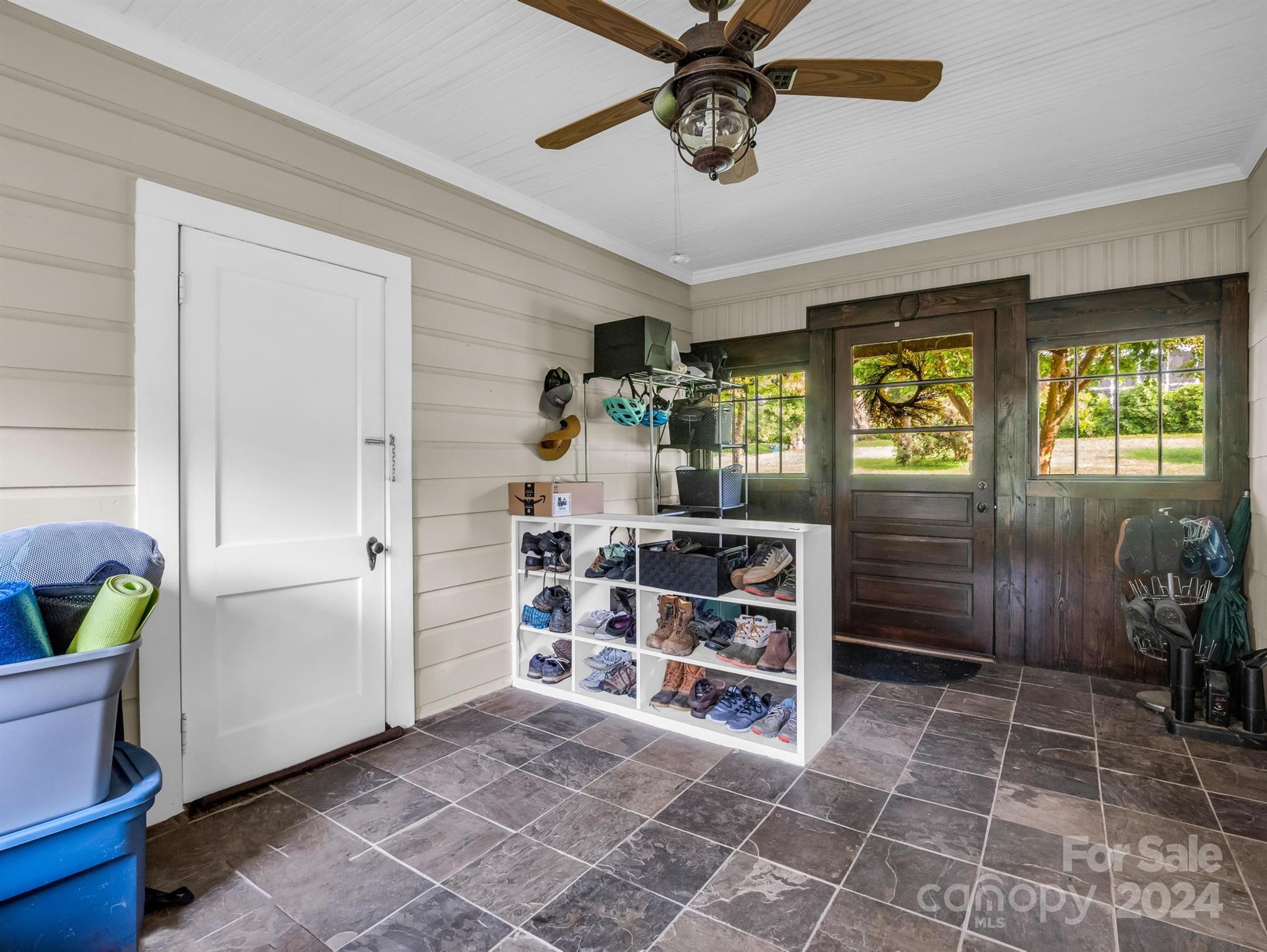 Mudroom with tiled floor, dark wood entry door, and shoe cubby filled with footwear