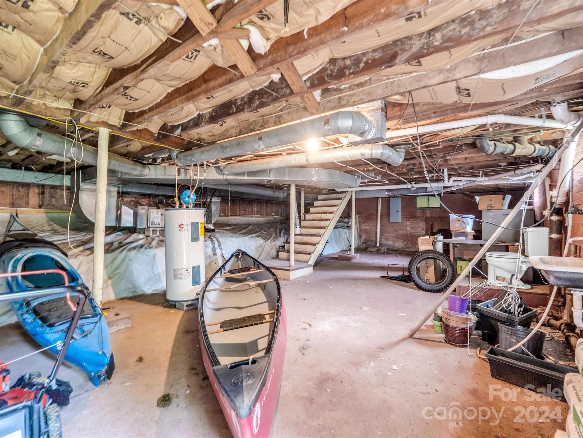 Unfinished basement with exposed joists, visible ductwork, stairs, and kayaks.
