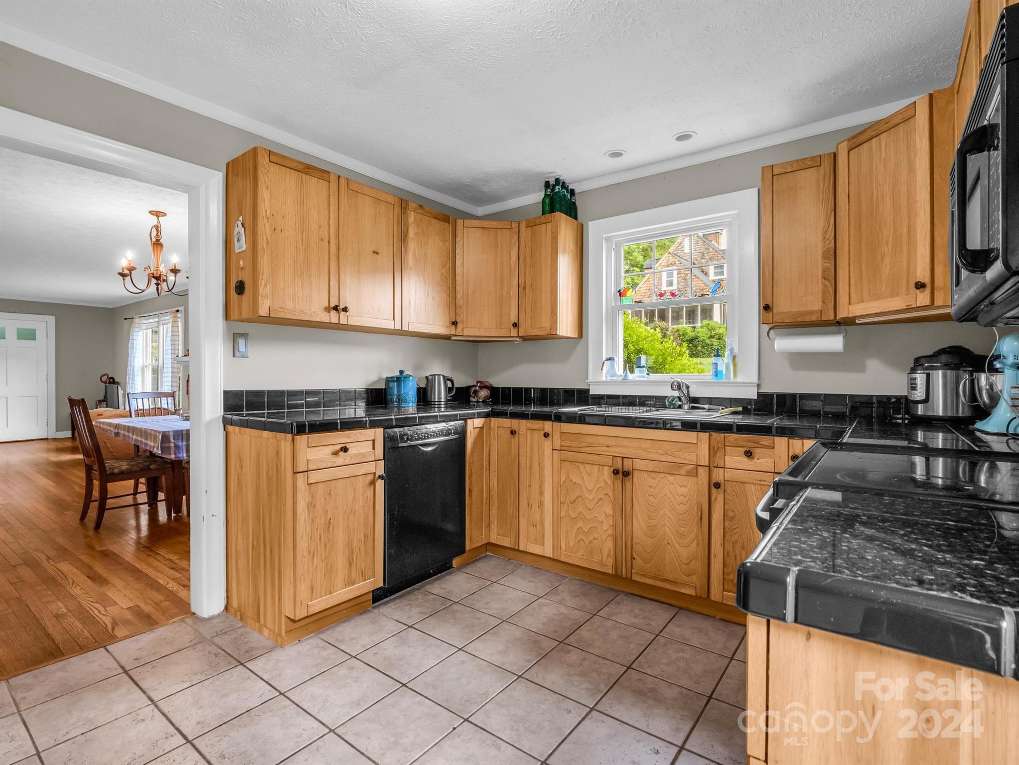 Kitchen with honey-colored wood cabinets, black countertops, tiled floor, and a window above the sink.