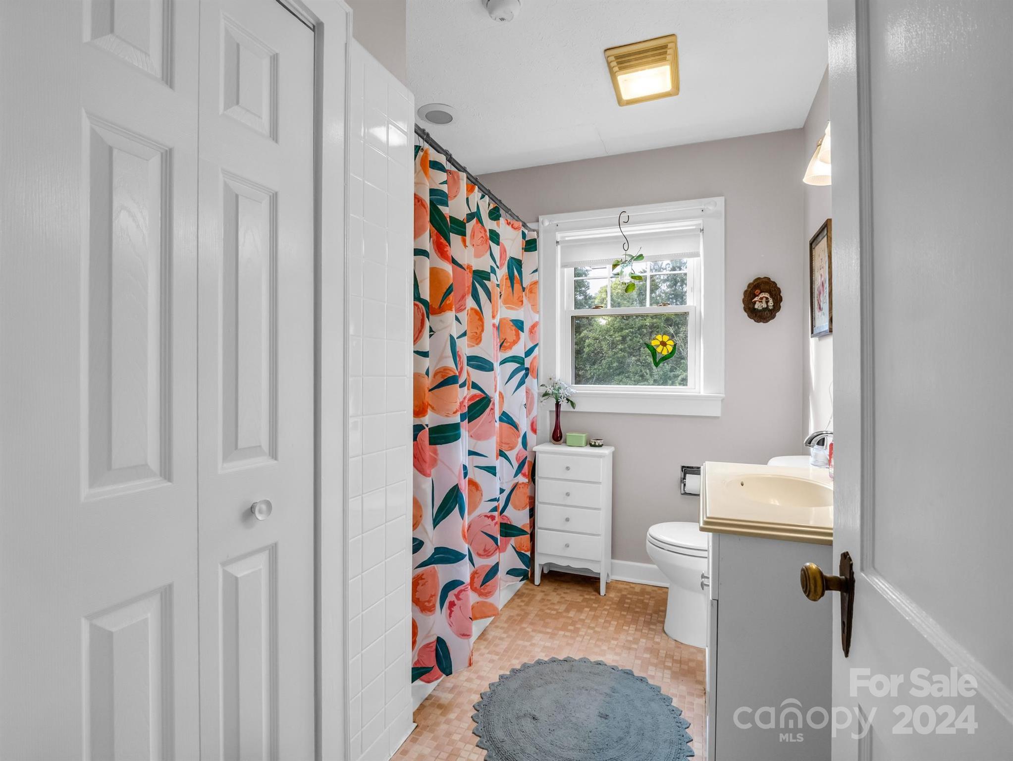 Bathroom with a colorful floral shower curtain, white vanity, and window overlooking trees.